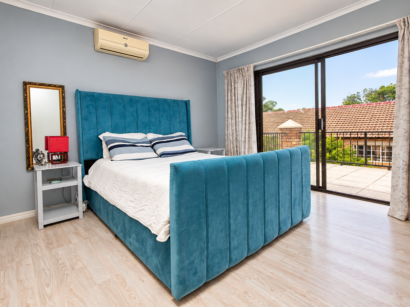A well-maintained bedroom featuring light laminate flooring, a split-system air conditioner, and large sliding glass doors providing access to a private balcony.