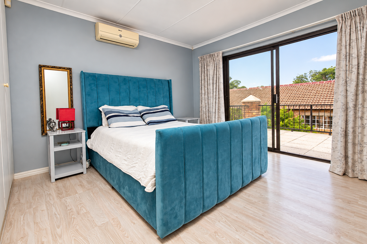 A well-maintained bedroom featuring light laminate flooring, a split-system air conditioner, and large sliding glass doors providing access to a private balcony.
