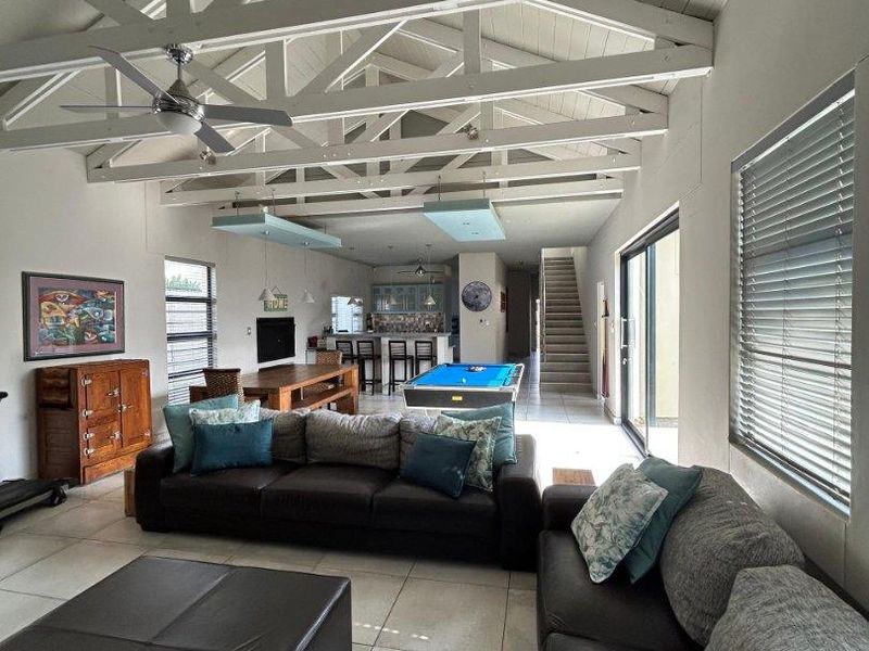 Spacious open-plan living area featuring a high vaulted ceiling with exposed trusses, tiled flooring, and seamless flow to the kitchen and dining space.