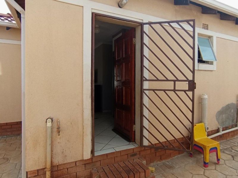 Rear exterior view showing a security gate, timber door, and tiled threshold with visible wear to the exterior wall plaster and paintwork.