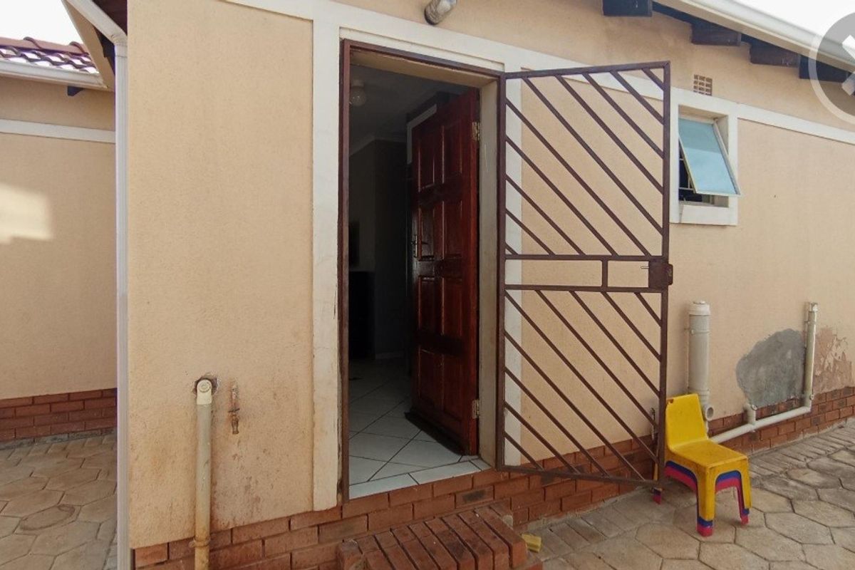 Rear exterior view showing a security gate, timber door, and tiled threshold with visible wear to the exterior wall plaster and paintwork.