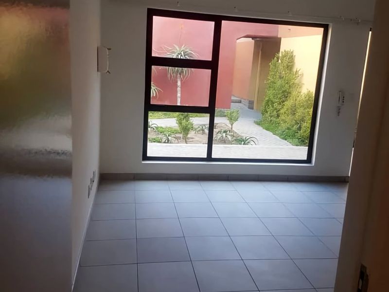 An empty living area featuring neutral tiled flooring, a large window with garden views, and an integrated intercom system.