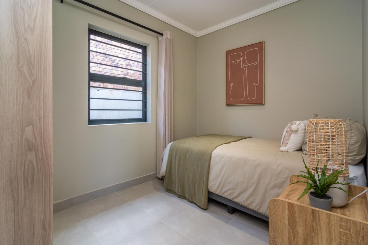 A well-maintained bedroom featuring neutral wall tones, tiled flooring, and a window fitted with security bars.