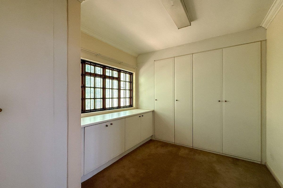 A bedroom featuring built-in wardrobes, low-level storage cabinetry, and a multi-pane window with a neutral color palette.
