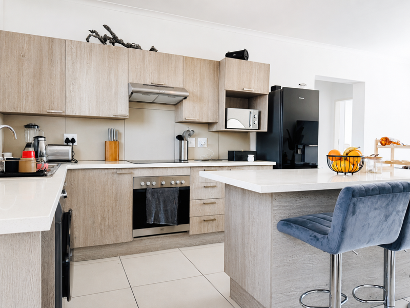 Modern kitchen featuring light wood-grain cabinetry, stone countertops, a central island, and integrated appliances including an oven and extractor fan.