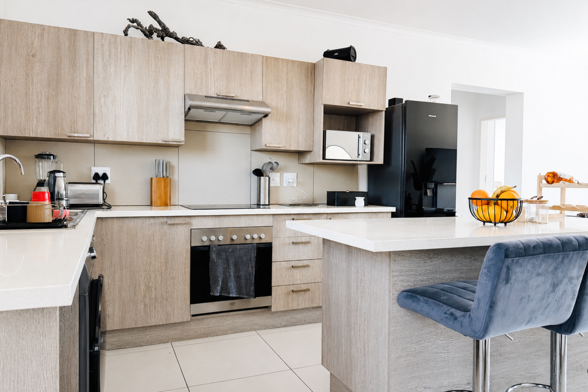 Modern kitchen featuring light wood-grain cabinetry, stone countertops, a central island, and integrated appliances including an oven and extractor fan.