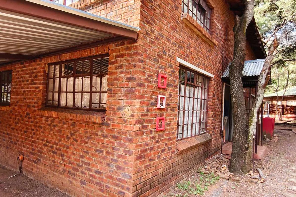 Exterior view of a face-brick house featuring a covered carport area, steel-framed windows, and a natural garden setting.
