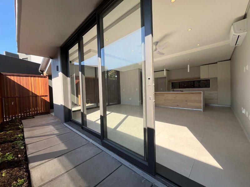Modern open-plan living and kitchen area featuring large sliding glass doors opening to a private patio, sleek cabinetry, and high-quality tiled flooring.