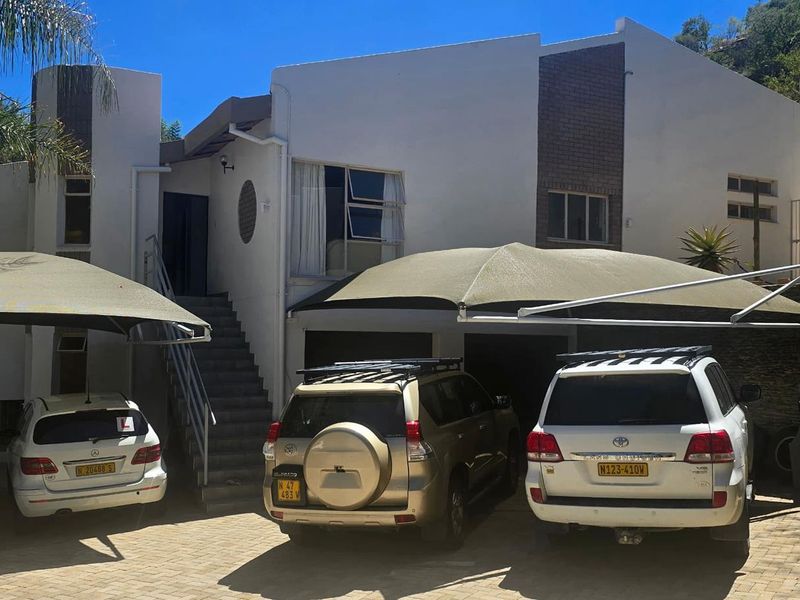 Front exterior view of the house featuring a paved driveway, multiple shade sail carports, and stone retaining walls.
