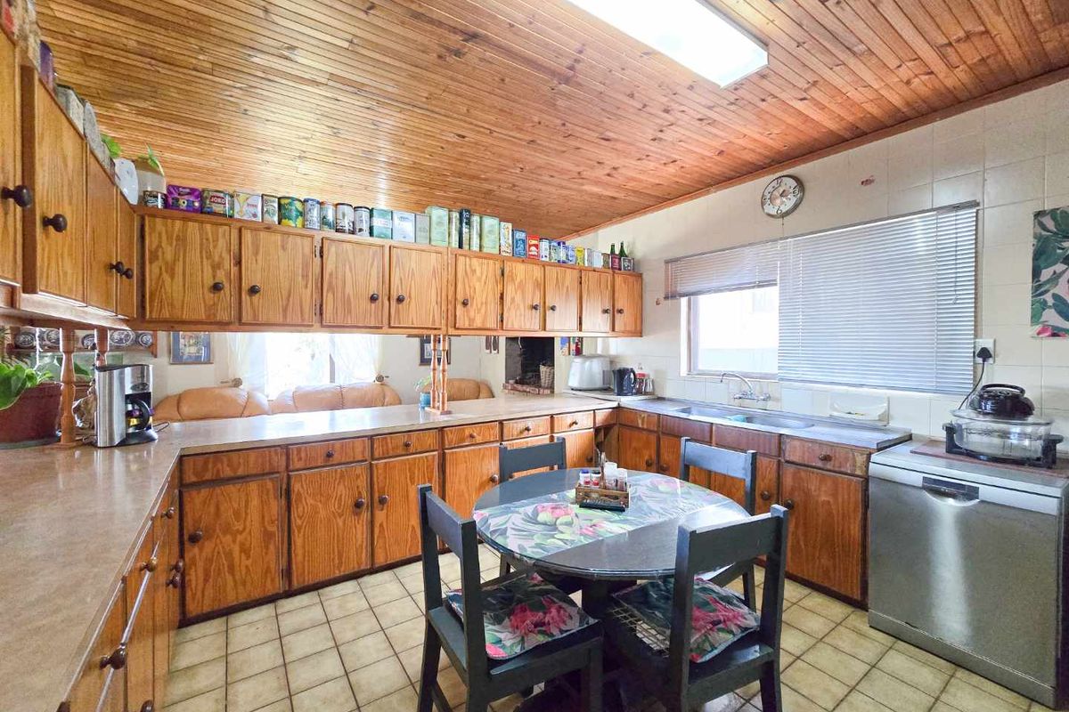 A dated kitchen featuring extensive wood cabinetry, tiled flooring, and a wood-paneled ceiling with a central skylight, offering a functional layout.