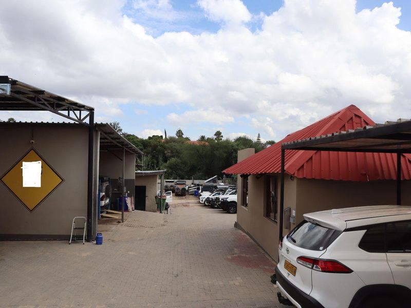 A paved outdoor yard area featuring a carport structure and access to multiple office or workshop buildings.