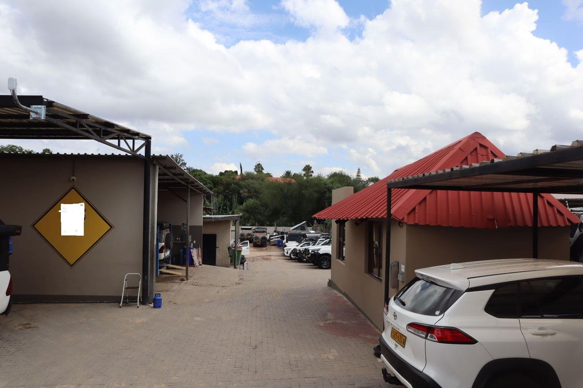 A paved outdoor yard area featuring a carport structure and access to multiple office or workshop buildings.