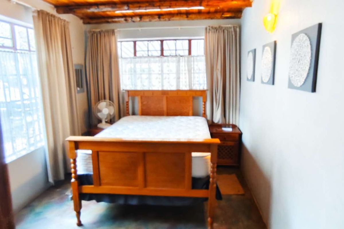 A cozy bedroom featuring exposed timber ceiling beams, large windows with natural light, and a neutral interior finish.