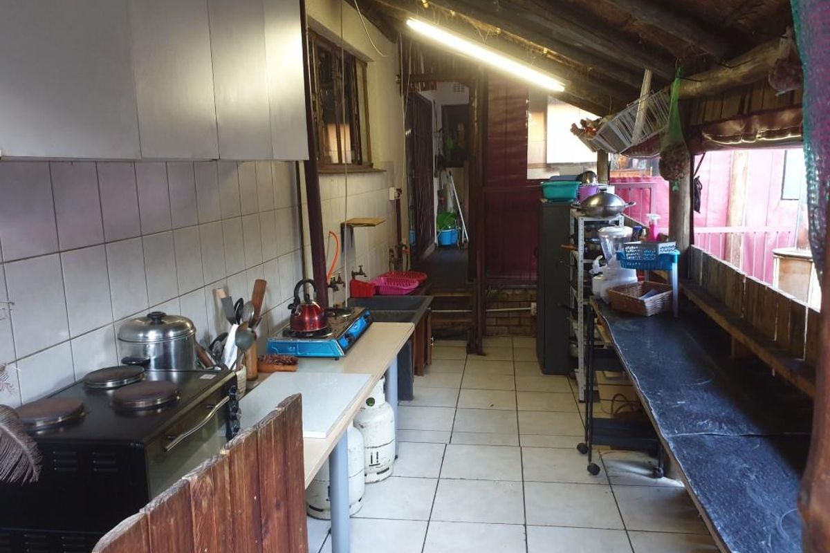A rustic, semi-enclosed kitchen area featuring tiled flooring, basic cabinetry, and exposed timber roof beams, providing a functional outdoor-style cooking space.