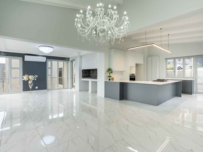 Spacious open-plan living and kitchen area featuring high-end marble-look flooring, modern cabinetry, a central island, and seamless access to outdoor spaces.