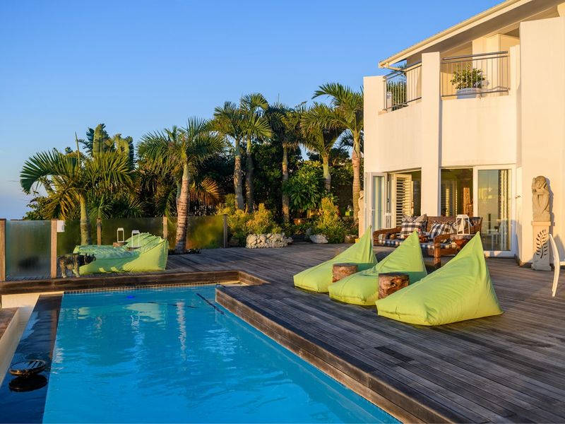 Outdoor pool area featuring timber decking, a swimming pool, and a glass balustrade, with direct access to the main house via sliding doors.