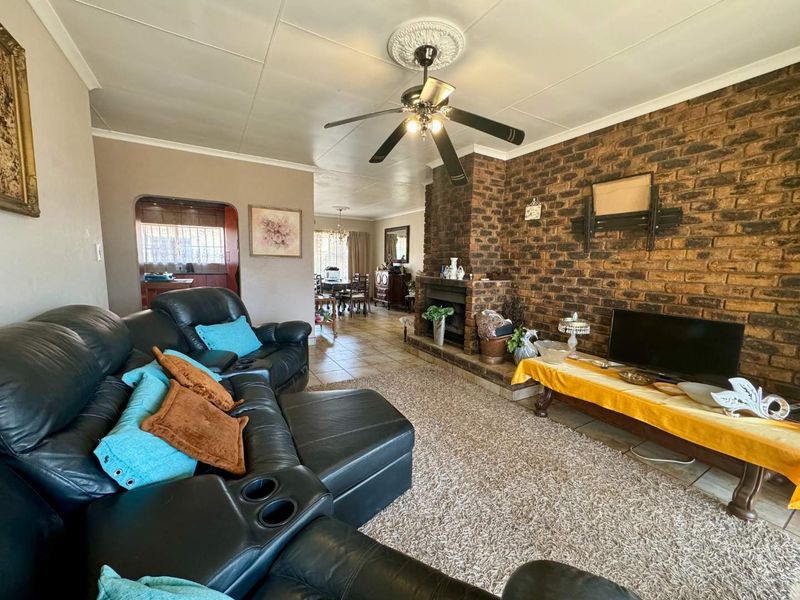 Spacious living room featuring a prominent brick fireplace, tiled flooring, and a ceiling fan, with an open flow into the adjacent dining area.