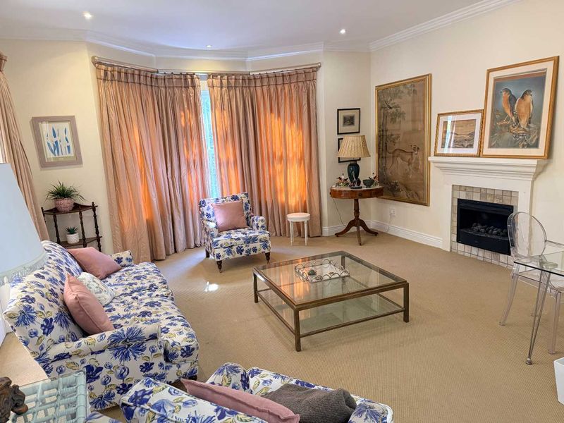 A well-maintained living room featuring a fireplace with a tiled surround, crown molding, recessed lighting, and a large bay window with floor-to-ceiling curtains.