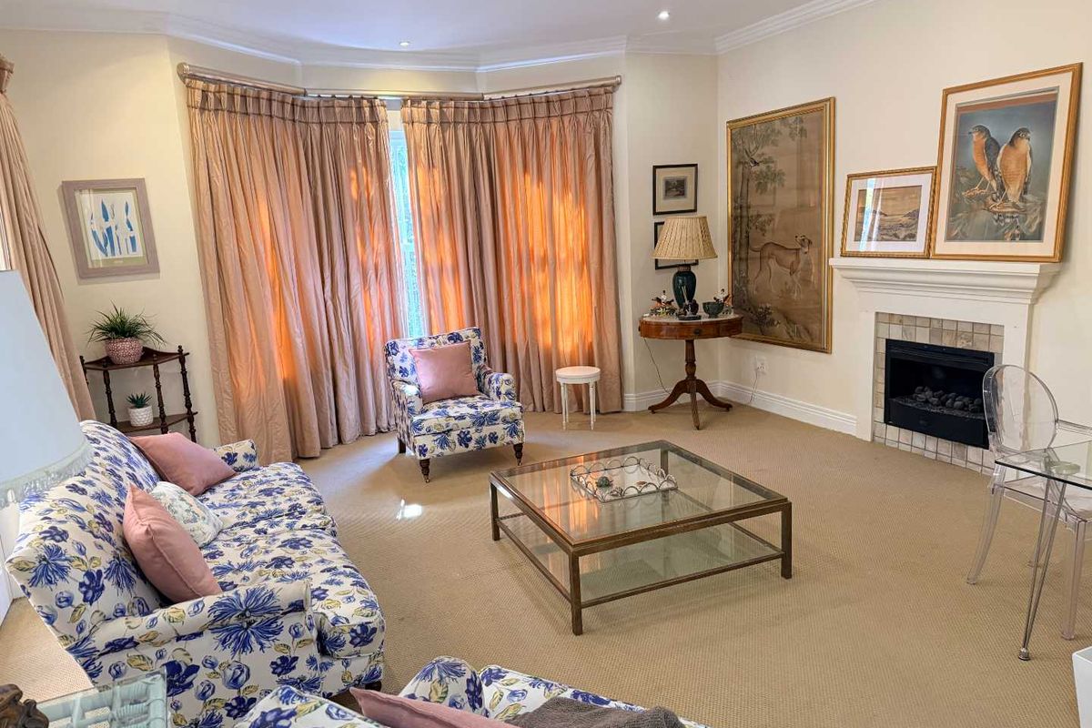 A well-maintained living room featuring a fireplace with a tiled surround, crown molding, recessed lighting, and a large bay window with floor-to-ceiling curtains.