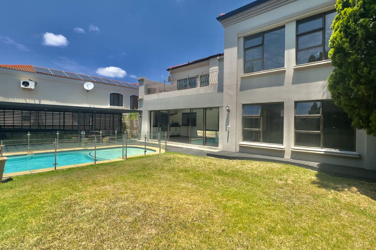 Rear view of the property featuring a swimming pool with glass balustrades, a manicured lawn, and a covered patio area.