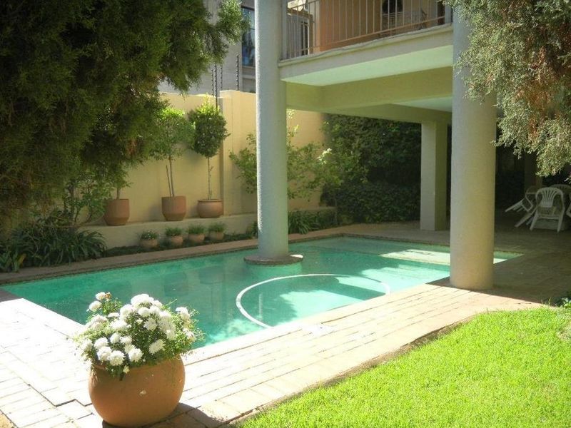 A private swimming pool area featuring structural support columns, a paved patio surround, and a raised garden bed with a retaining wall.