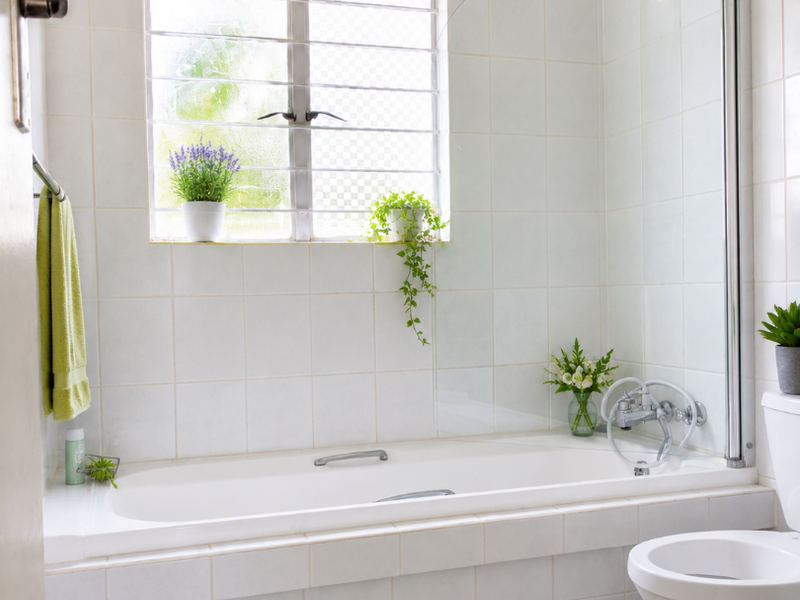 A functional bathroom featuring a built-in bathtub with a glass shower screen, ceramic tiling, and a standard toilet.