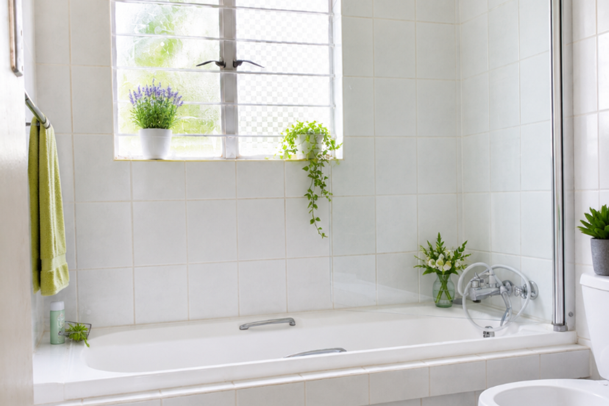 A functional bathroom featuring a built-in bathtub with a glass shower screen, ceramic tiling, and a standard toilet.