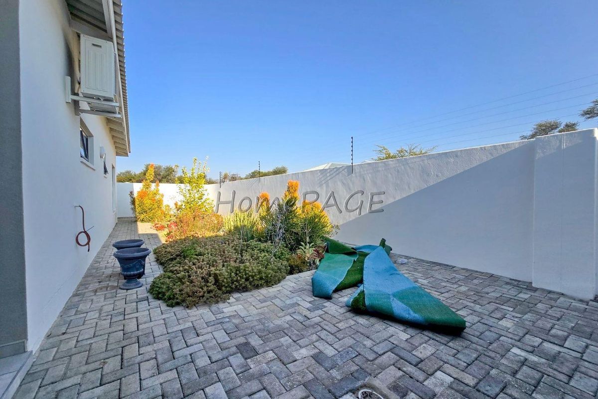 A paved rear courtyard area featuring a perimeter boundary wall with electric fencing and a small landscaped garden section.