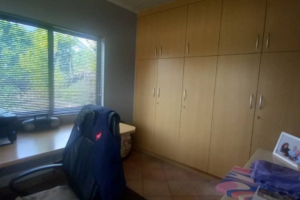 A functional bedroom featuring extensive built-in wooden cupboards, tiled flooring, and large windows with venetian blinds, offering ample storage space.