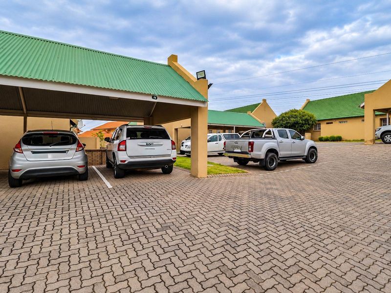 A paved communal parking area featuring covered carports with green corrugated metal roofing, providing convenient sheltered parking for residents.