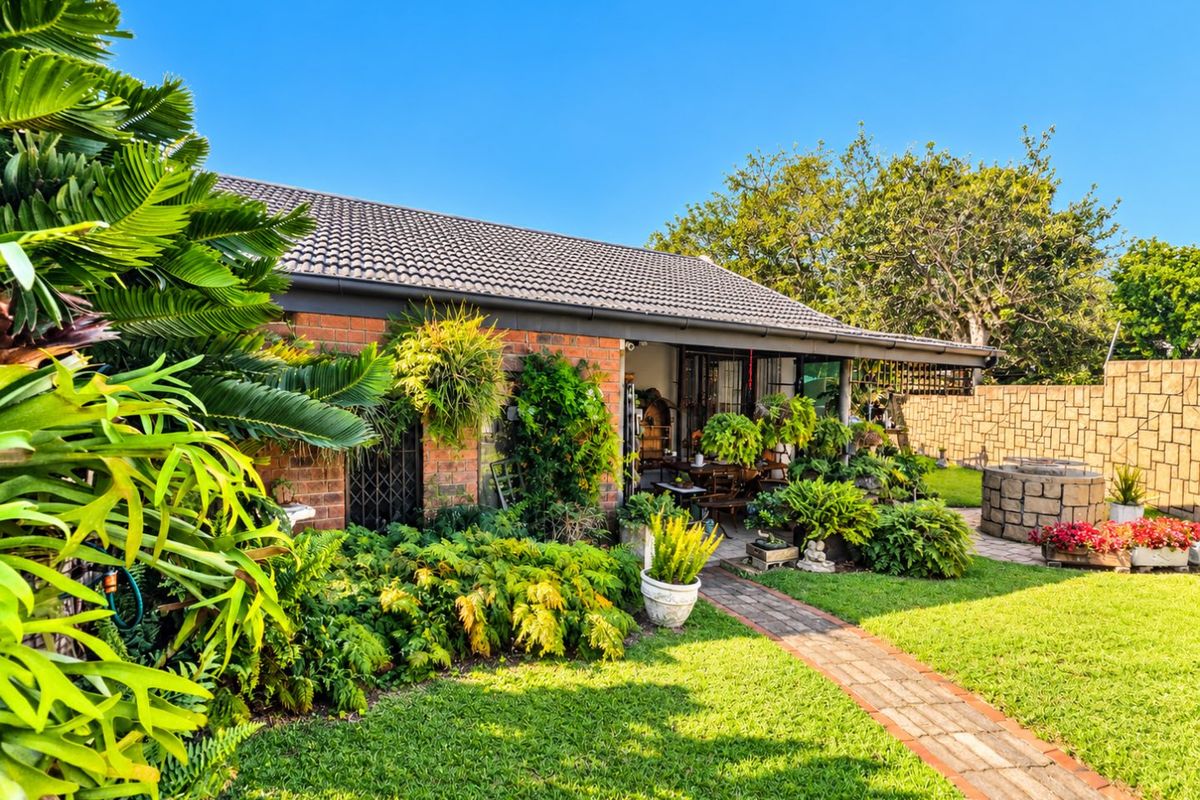 A well-maintained rear garden featuring a brick facade, tiled roof, paved pathway, and a stone-clad fire pit area.