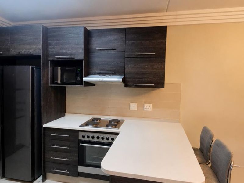 Modern kitchen featuring dark wood cabinetry, white stone countertops, integrated appliances including an oven and hob, and a breakfast bar peninsula.