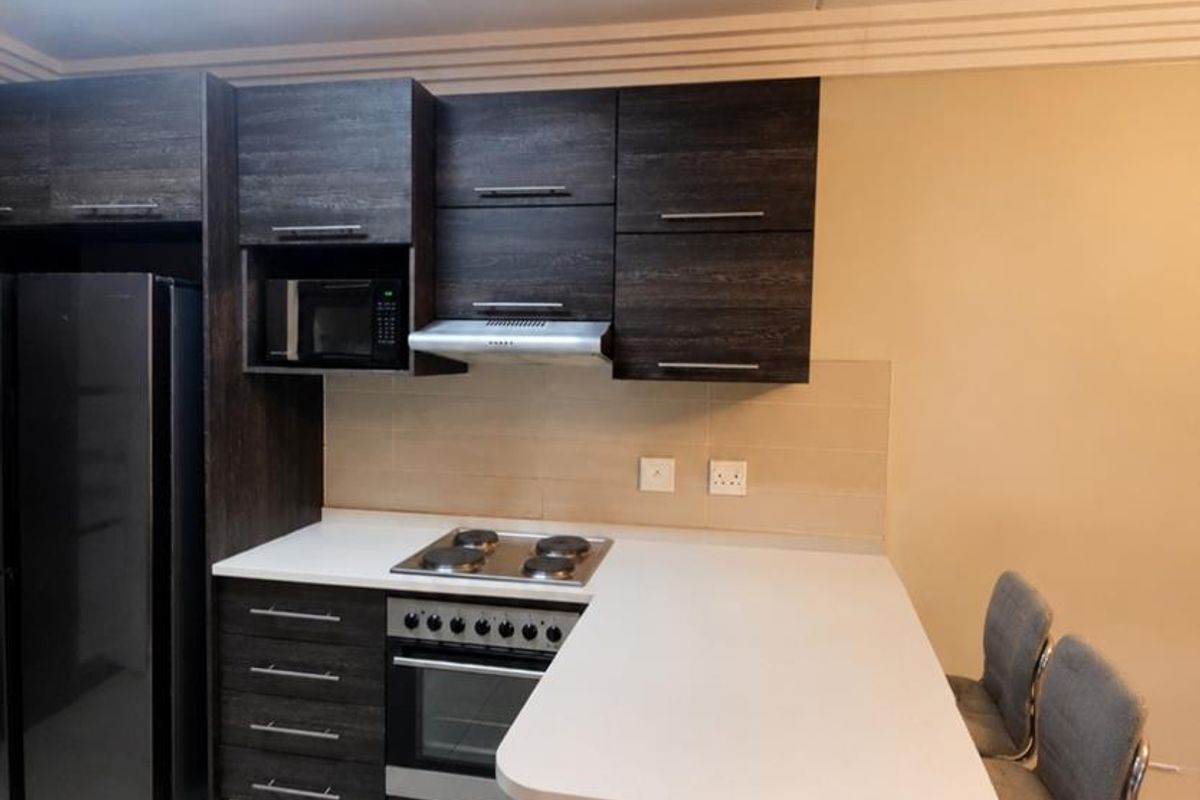 Modern kitchen featuring dark wood cabinetry, white stone countertops, integrated appliances including an oven and hob, and a breakfast bar peninsula.