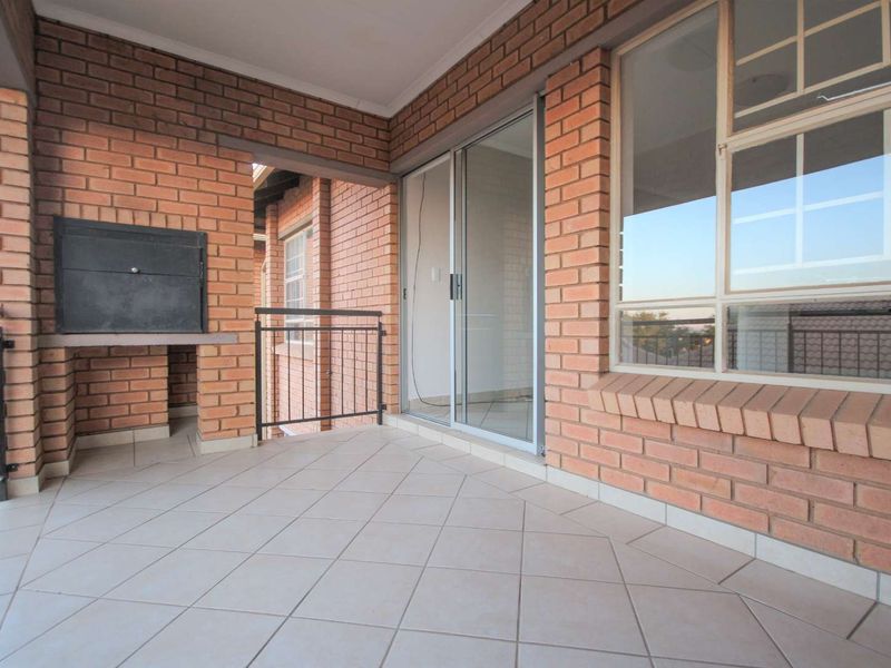 A covered balcony featuring face-brick walls, tiled flooring, and a built-in braai, providing an ideal space for outdoor entertaining.