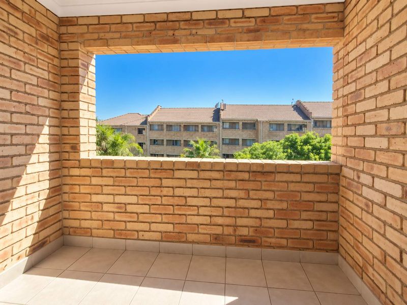A private balcony featuring exposed brick walls and tiled flooring, offering an open outlook over the surrounding apartment complex.