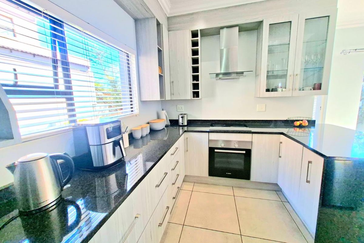 Modern kitchen featuring granite countertops, built-in oven, extractor fan, and ample fitted cabinetry with glass-fronted display units and tiled flooring.