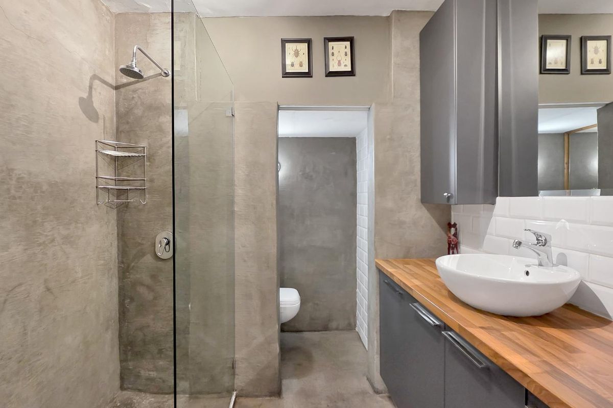Modern bathroom featuring a walk-in shower with glass screen, vessel sink on a wooden vanity, and a separate toilet area with concrete-style wall finishes.
