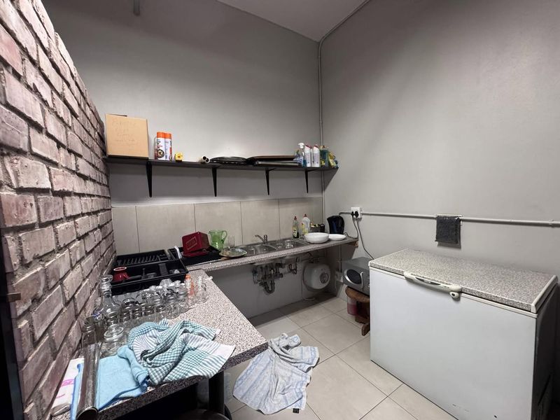 Functional scullery area featuring a stainless steel sink, laminate countertops, wall-mounted shelving, and an exposed brick feature wall.
