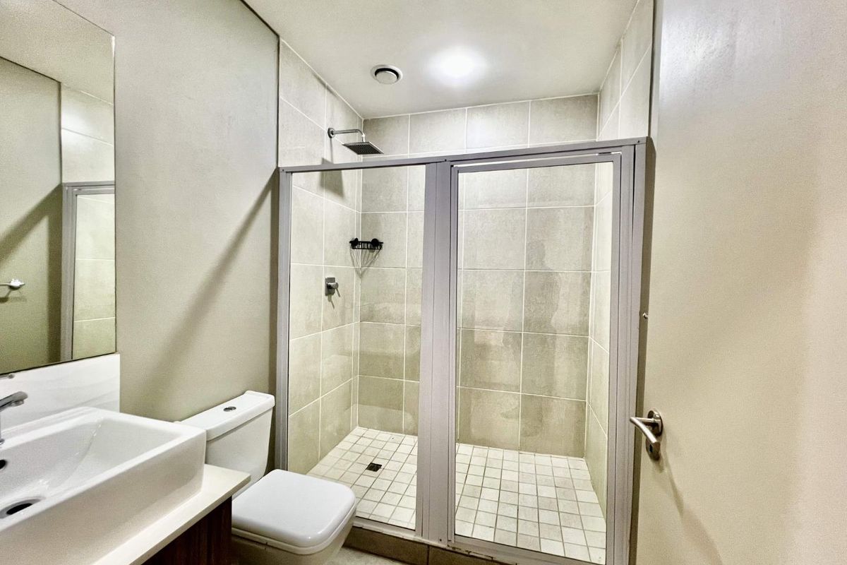 A modern bathroom featuring a walk-in shower with glass enclosure, a vanity basin, and a toilet, finished with neutral wall and floor tiling.