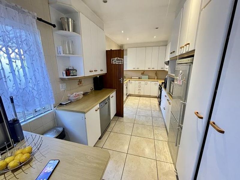 A functional kitchen featuring white cabinetry, light-toned laminate countertops, tiled flooring, and integrated appliances, offering a clean and practical workspace.