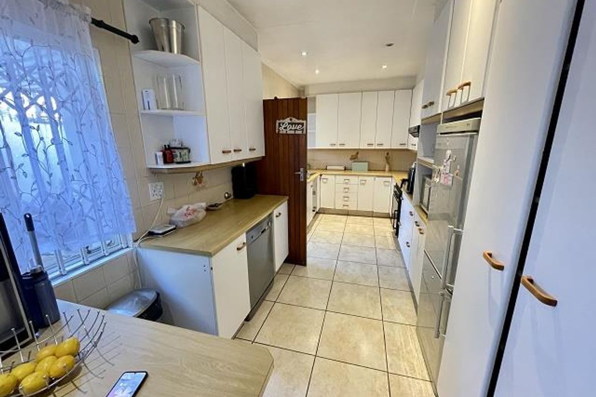 A functional kitchen featuring white cabinetry, light-toned laminate countertops, tiled flooring, and integrated appliances, offering a clean and practical workspace.