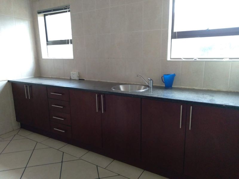 A functional scullery area featuring dark wood cabinetry, granite countertops, a stainless steel sink, and tiled splashbacks.