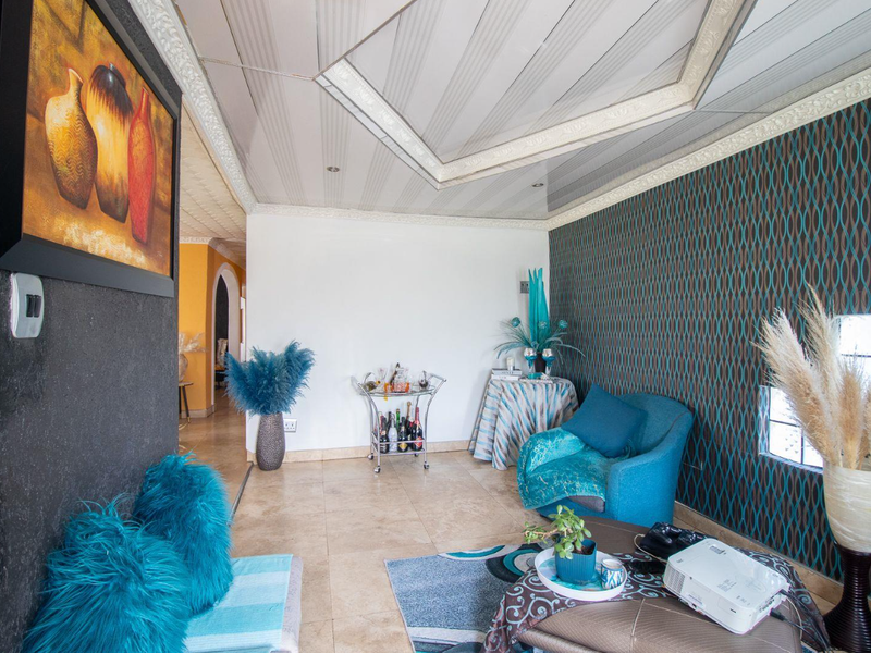 A living room featuring tiled flooring, decorative ceiling panels, and a feature wall with patterned wallpaper.
