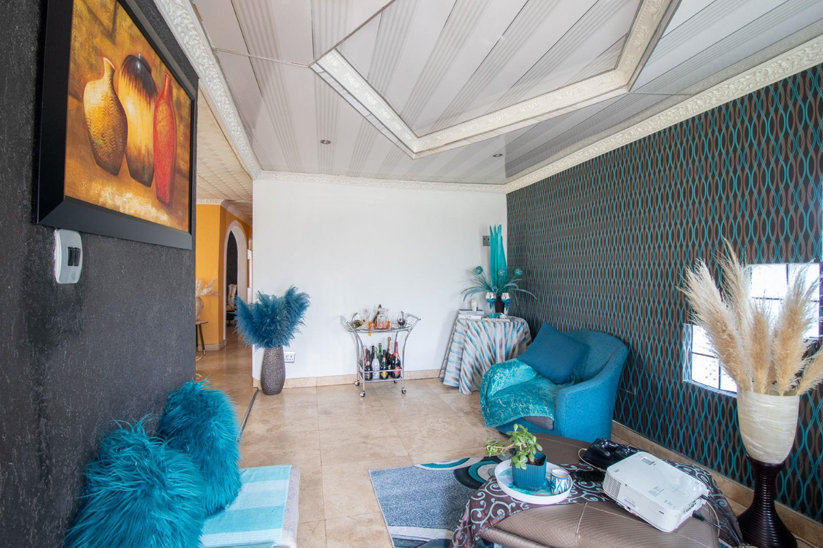 A living room featuring tiled flooring, decorative ceiling panels, and a feature wall with patterned wallpaper.