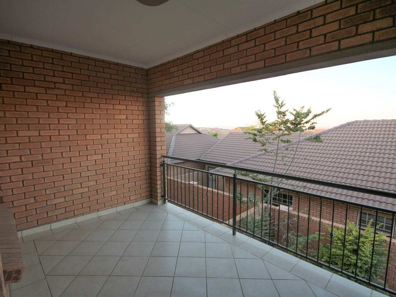 A covered balcony featuring exposed brick walls, tiled flooring, and a metal balustrade, offering an open view of the surrounding residential area.