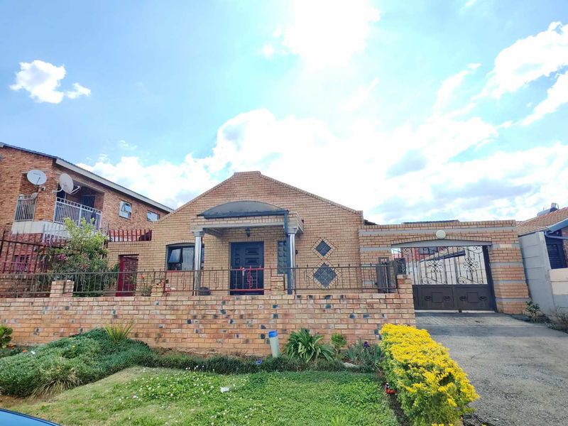 Front elevation of a face brick house featuring a paved driveway, secure wrought iron perimeter fencing, and a covered entrance porch.