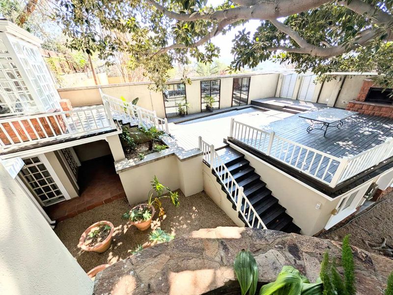 A multi-level rear outdoor entertainment area featuring timber decking, a built-in fireplace, and a gravel courtyard with stairs connecting the levels.