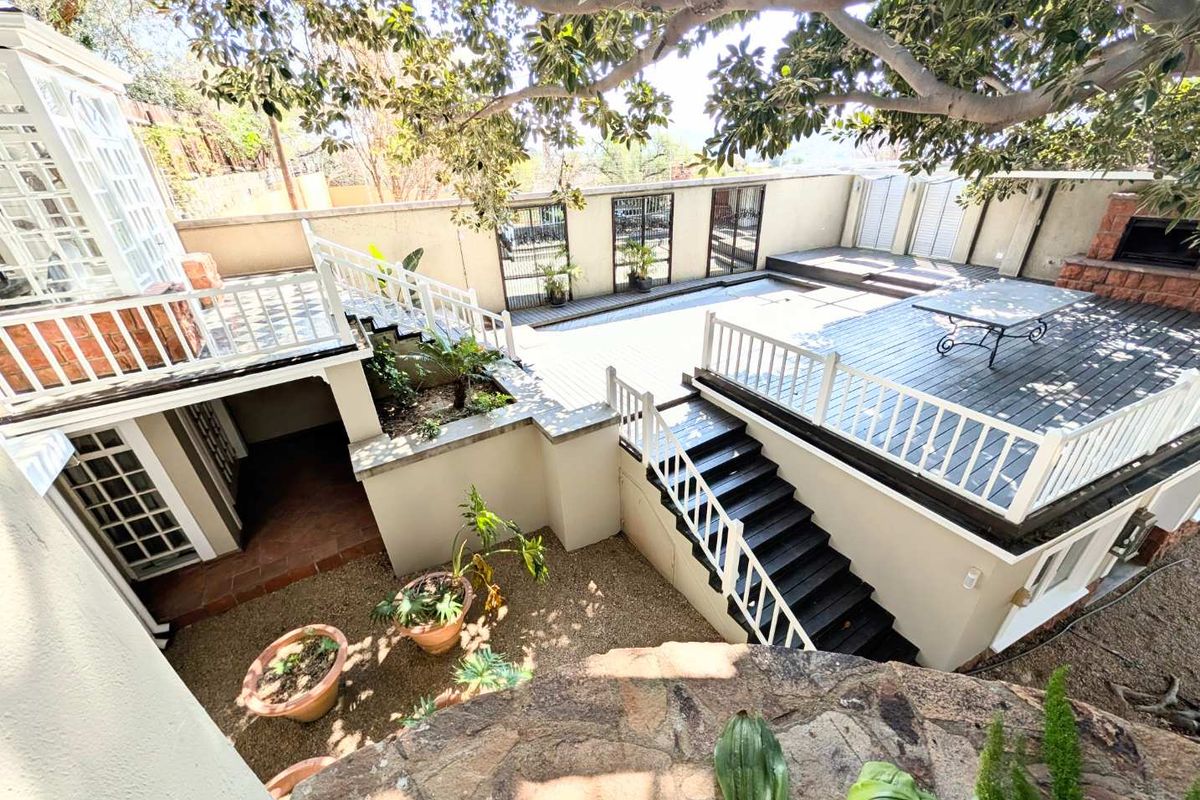 A multi-level rear outdoor entertainment area featuring timber decking, a built-in fireplace, and a gravel courtyard with stairs connecting the levels.
