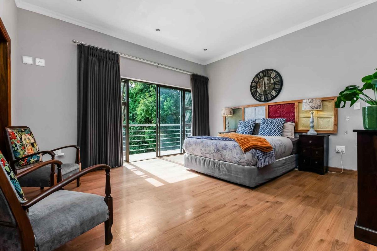 Spacious bedroom featuring warm wood-look flooring, recessed ceiling lighting, and large sliding glass doors opening onto a private balcony with lush green views.