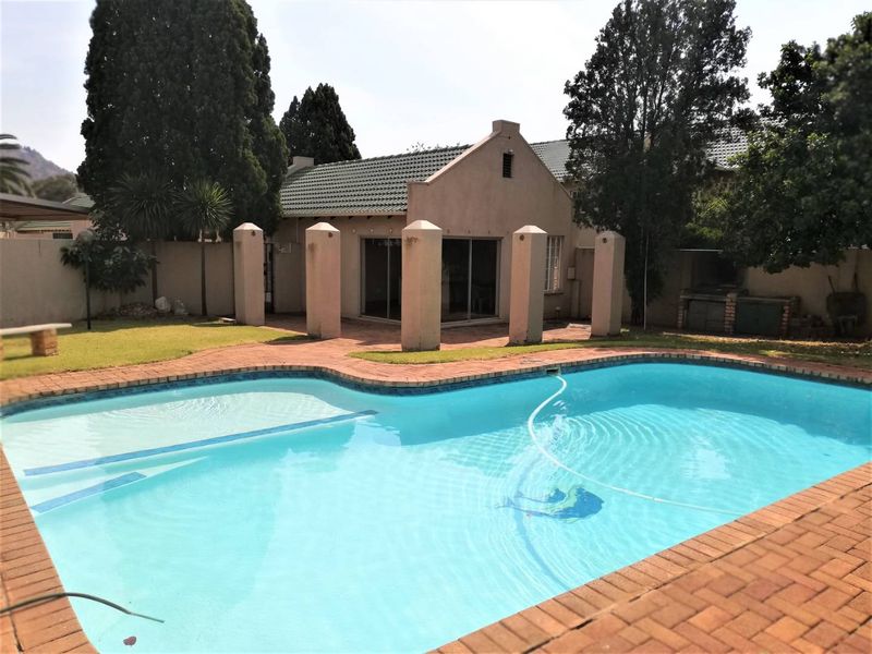 A private backyard featuring a swimming pool with brick paving, a built-in braai area, and a rear view of the townhouse structure.
